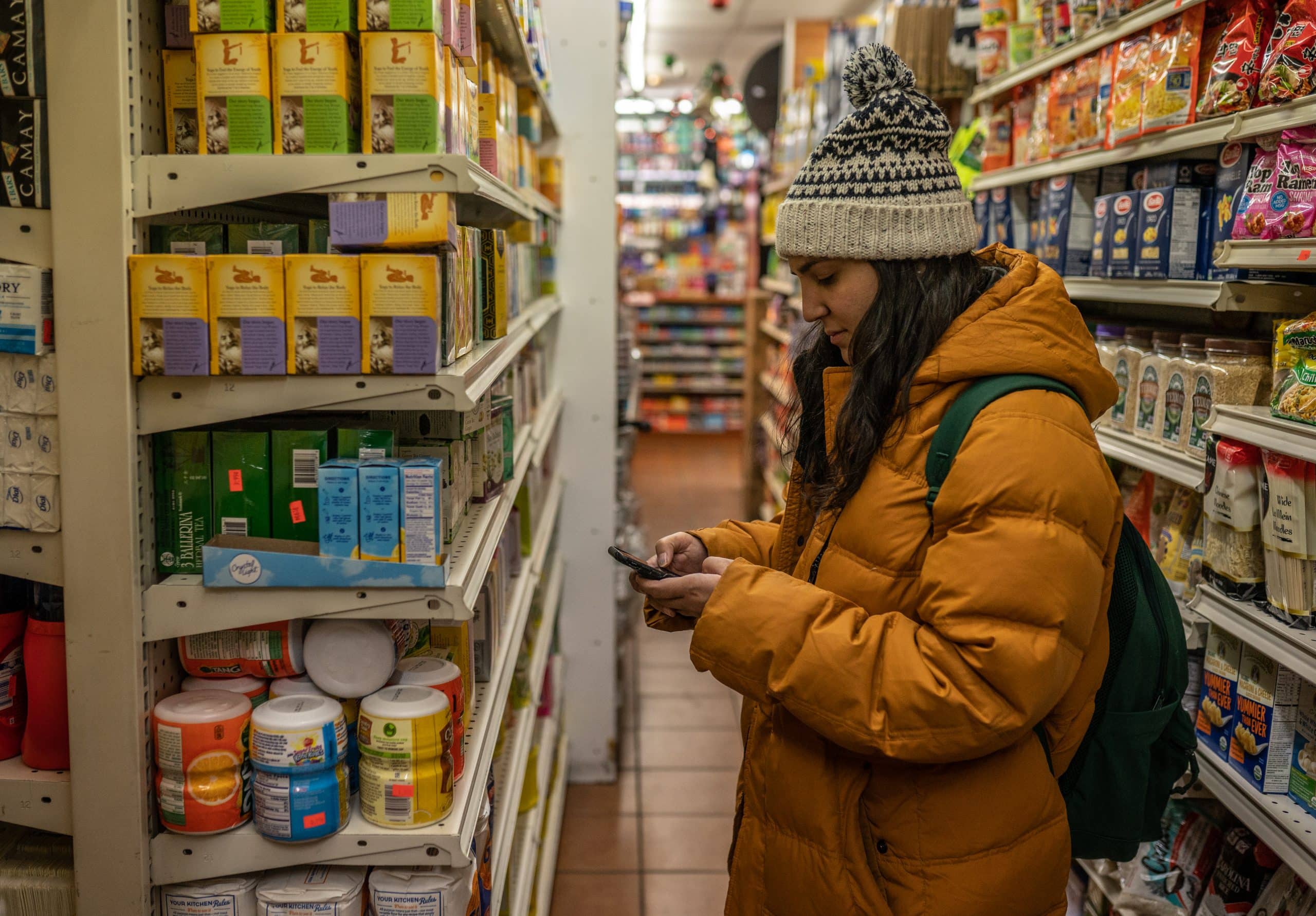 Woman in a coat looking at her phone in a grocery store