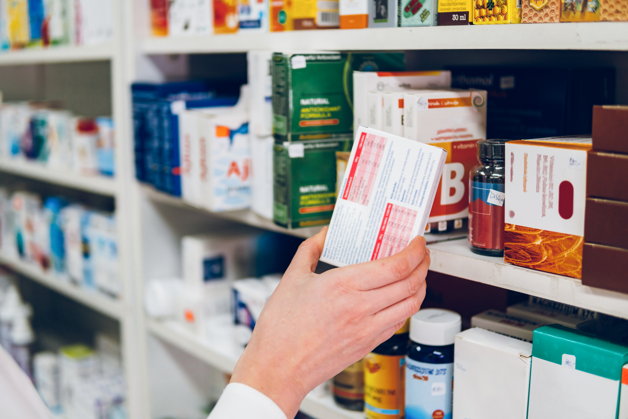 Brand name vs generic. A young female pharmacist arranges medicines on the shelves of the pharmacy and makes an inventory.