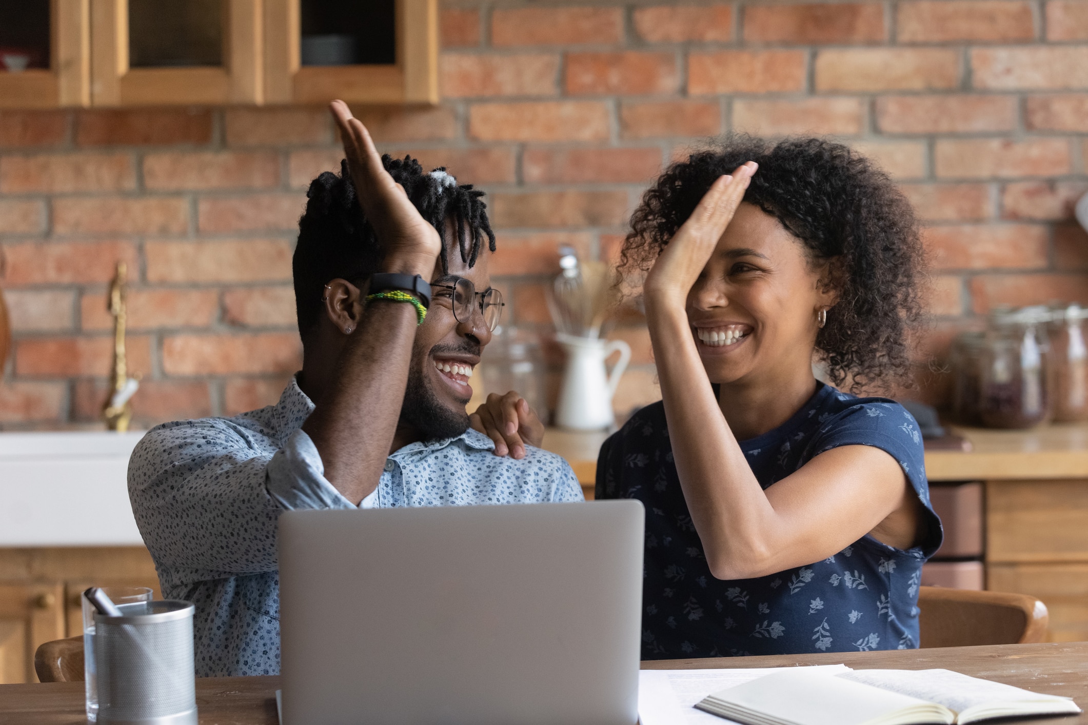 how to save on utility bills. Happy excited Black mixed race couple celebrating financial success at laptop, getting income, loan, mortgage bank approval, planning good family budget. Young husband and wife giving high five.