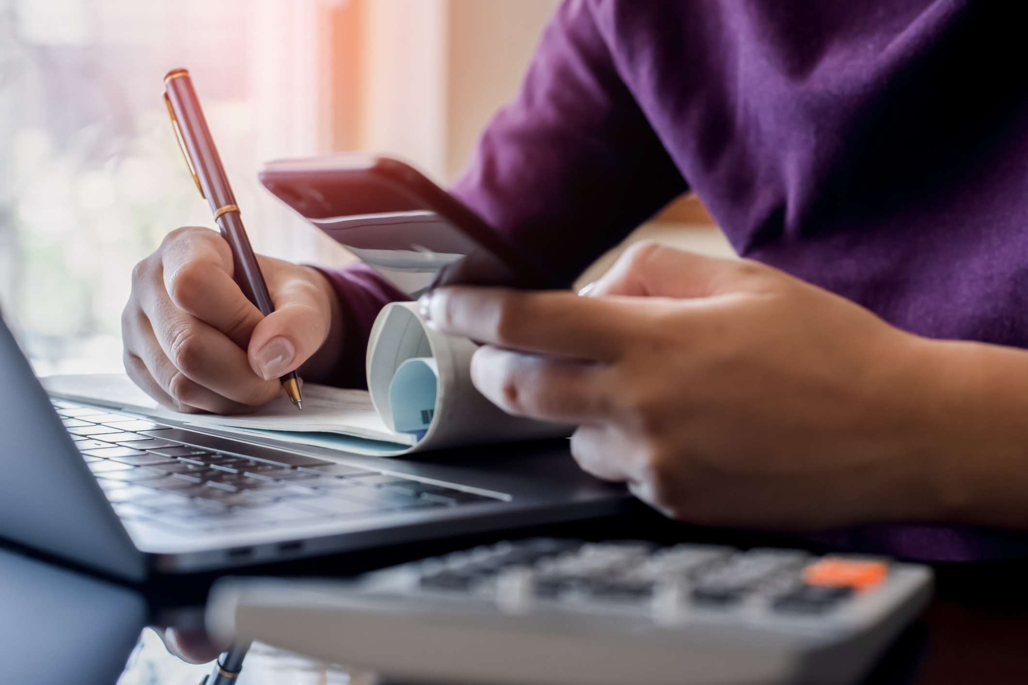 how to stop living paycheck to paycheck. Person with calculator and computer, taking notes.