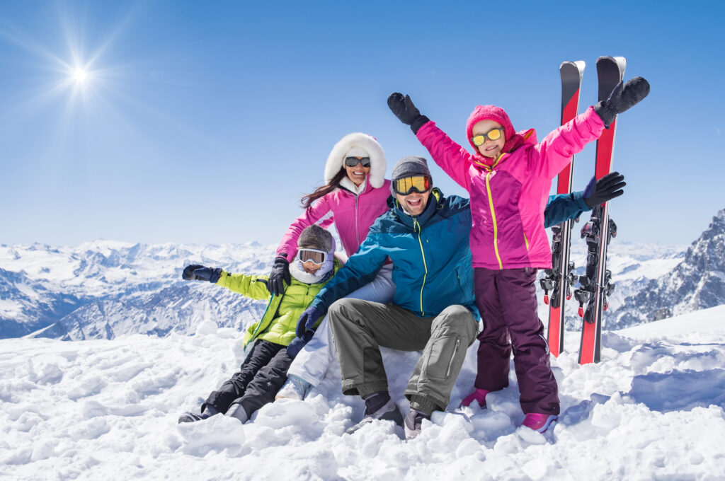 Family snow trip: Laughing family in winter vacation with ski sport on snowy mountains. Happy man and woman with sons having fun and looking at camera. Family with two children enjoying winter holiday at ski resort.