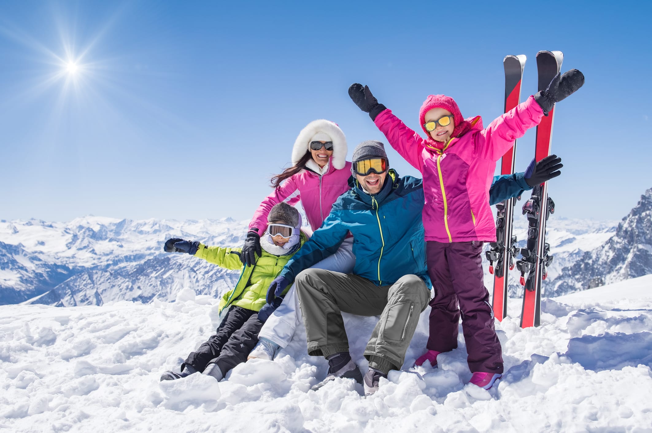 Family snow trip: Laughing family in winter vacation with ski sport on snowy mountains. Happy man and woman with sons having fun and looking at camera. Family with two children enjoying winter holiday at ski resort.