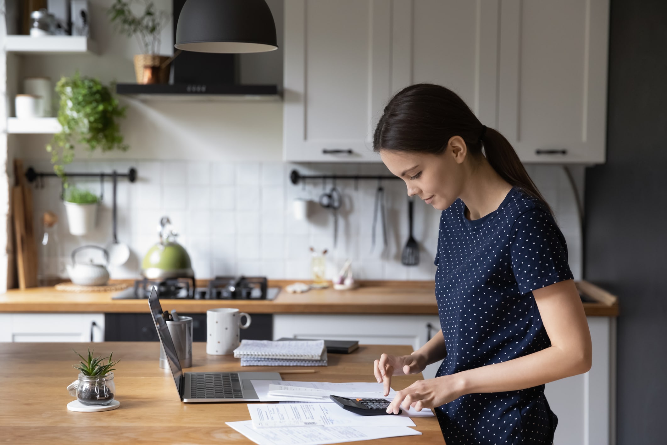 understanding your annual expenses. Woman at kitchen counter with computer and calculator.