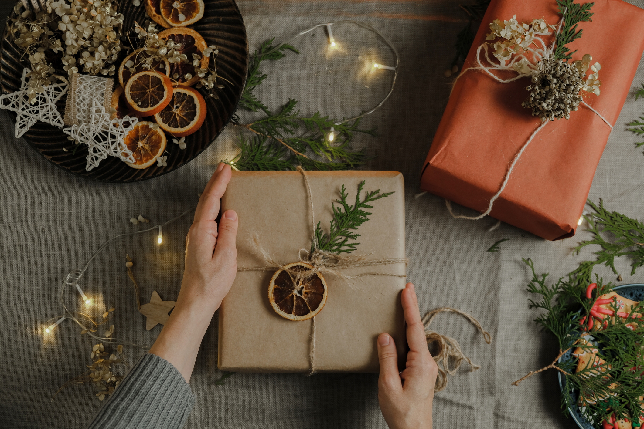 homemade holiday gifts. Female hands holds Christmas present wrapped in kraft paper. DIY Christmas packaging for holiday Christmas gifts. Table top view.