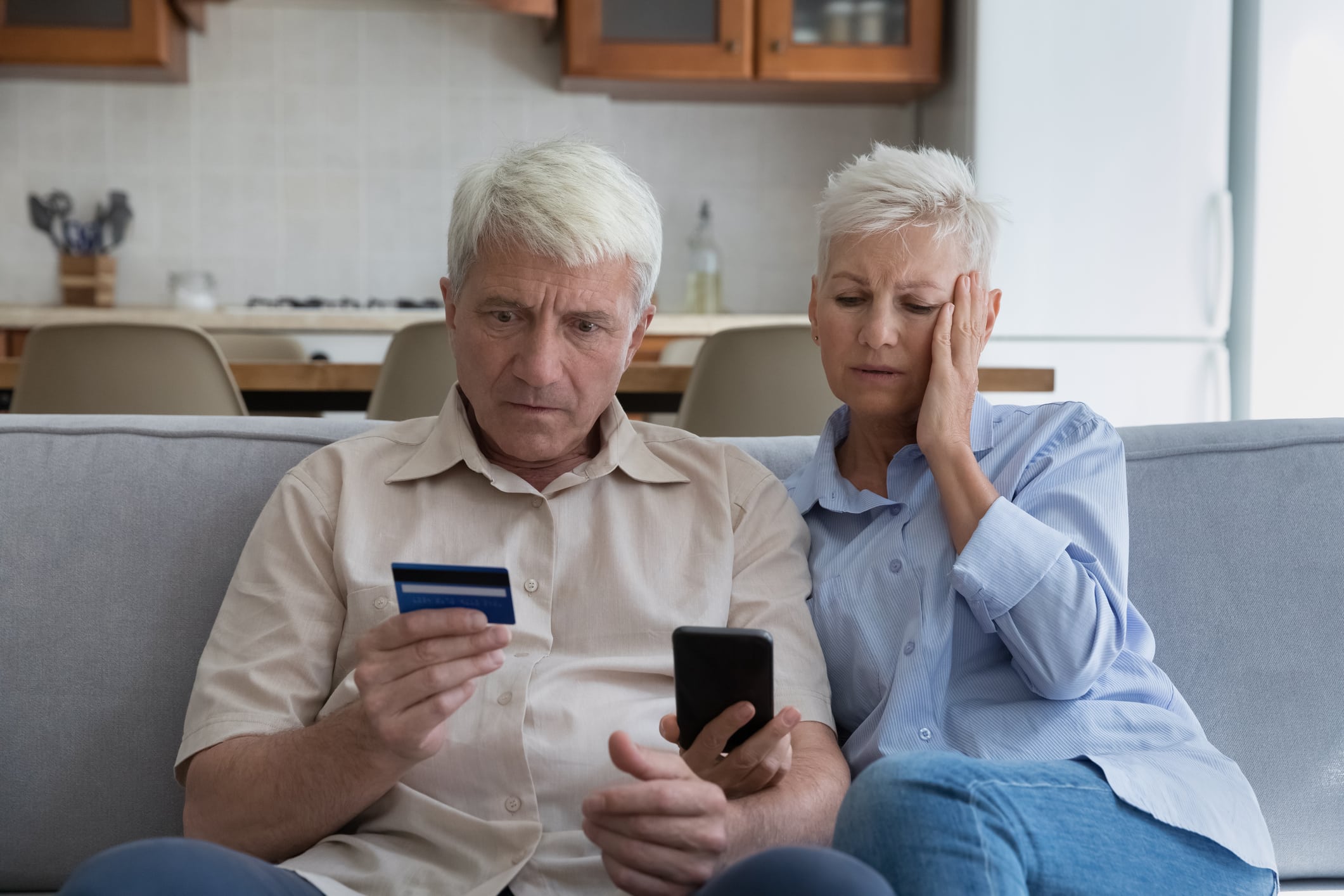 average credit card debt. Shocked aged couple become victims of online fraud using credit card phone to pay for goods order service online on suspicious website. Frustrated older spouses overspending money at internet shopping.