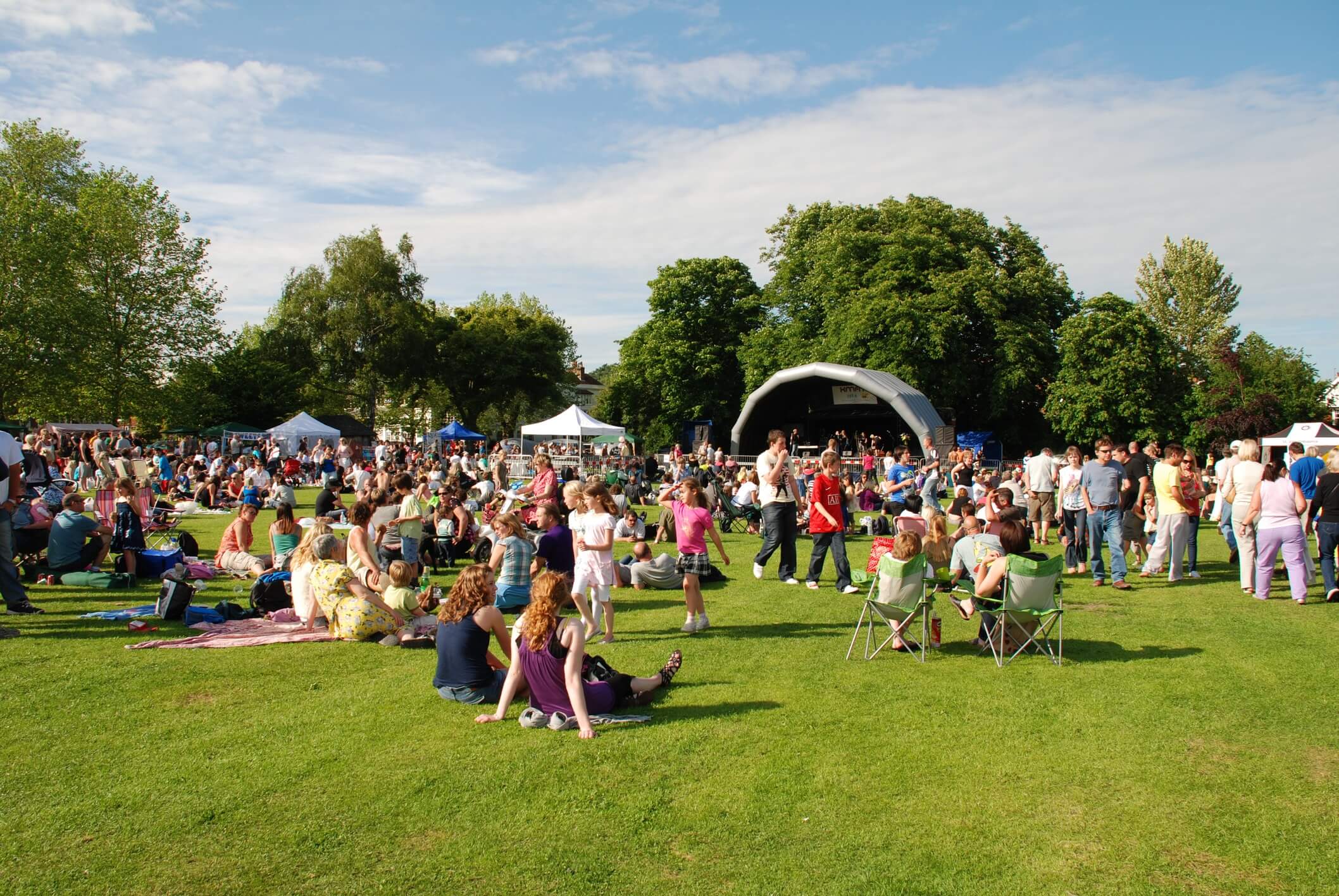 how to save money on entertainment. A music festival with people on the lawn and white tents.