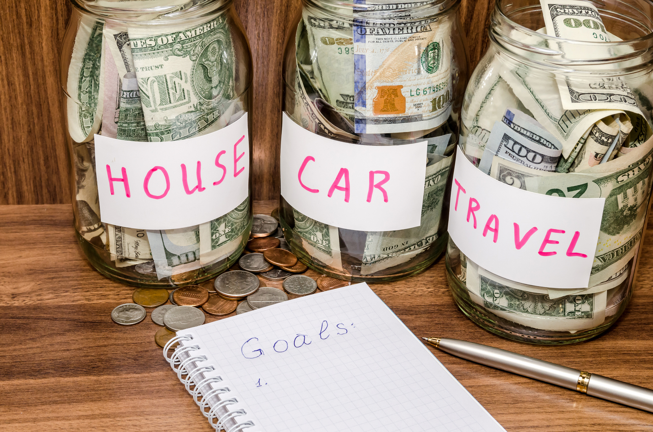 short term financial goals. jars of money labeled house, car, travel.