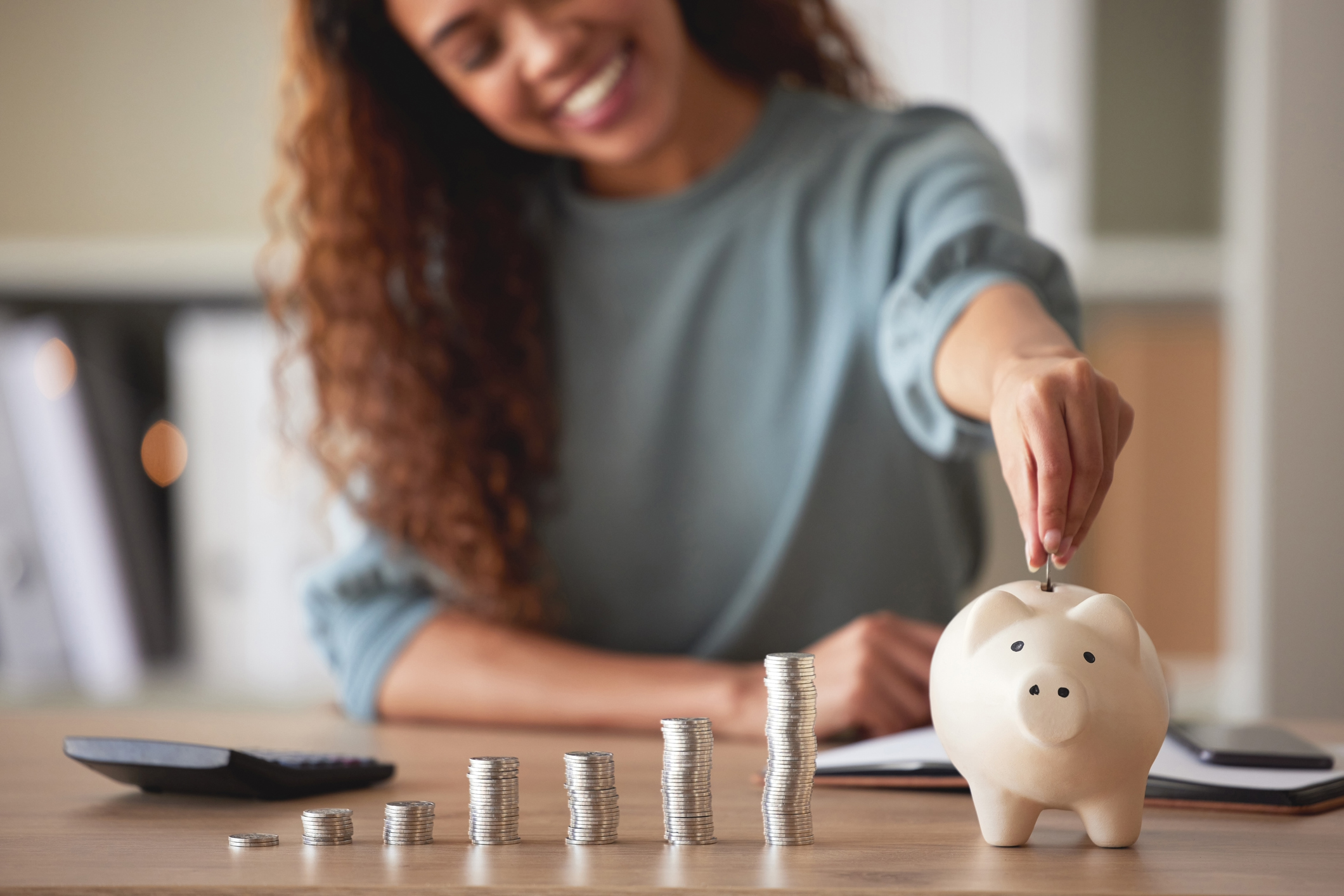 Young african american woman putting money in a piggy bank to save $10,000 a year.