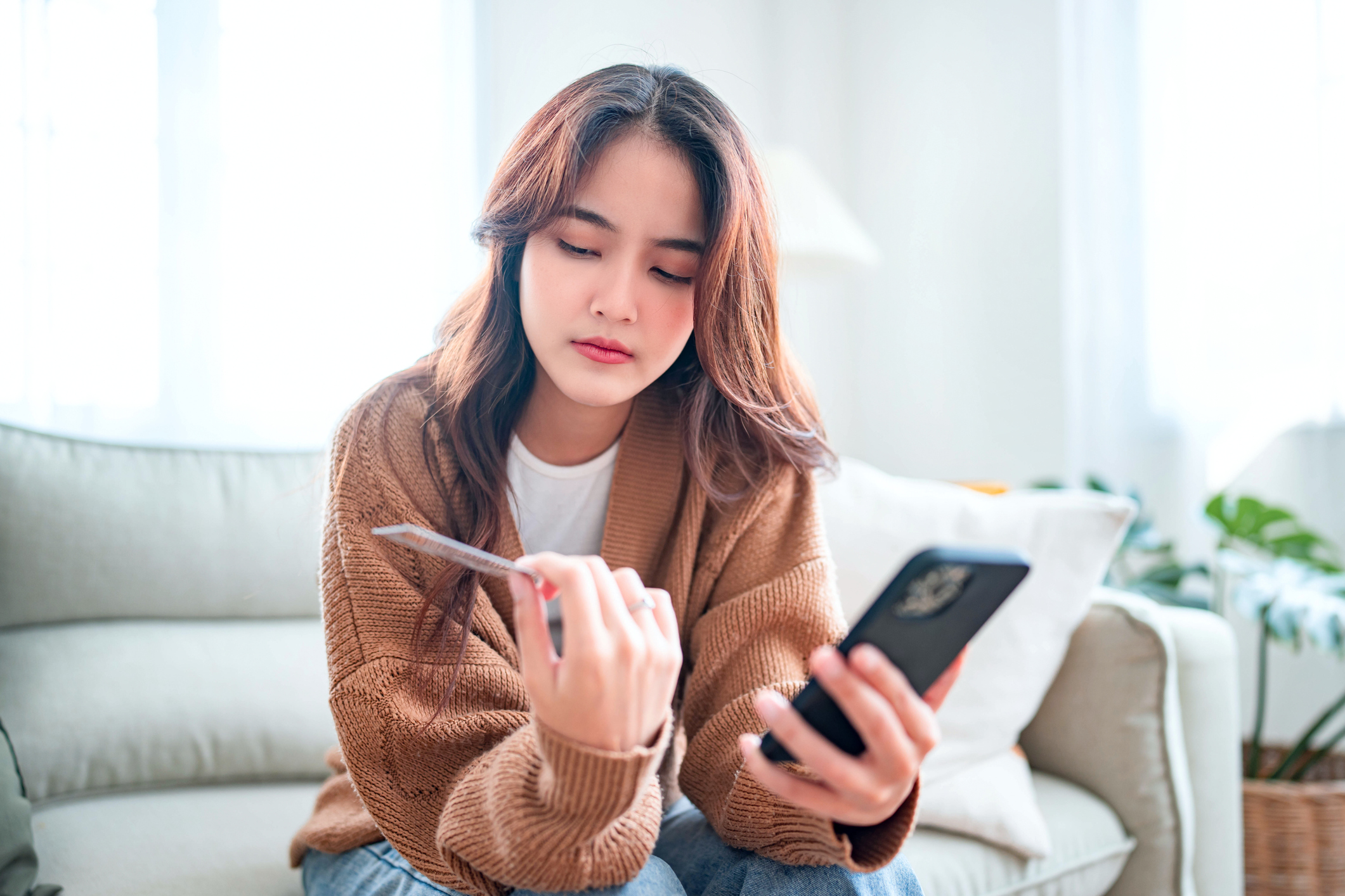 young asian woman looking at credit card wondering how to stop overspending