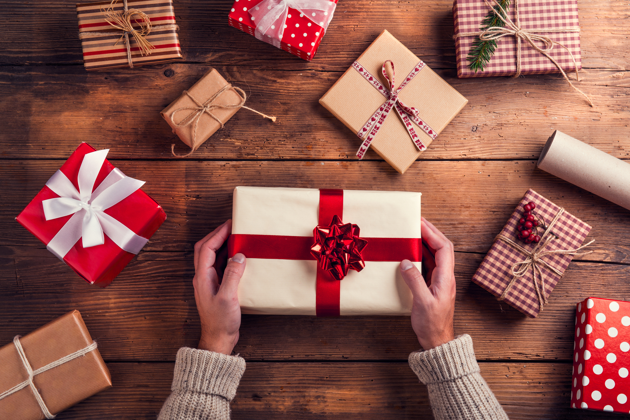 Last-minute gift ideas, man holding Christmas presents laid on a wooden table.