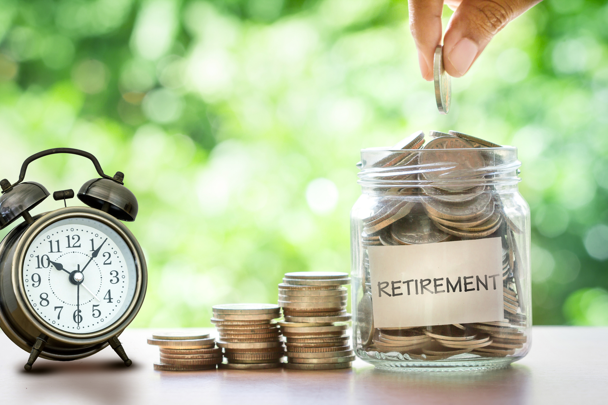 Hand putting Coins in glass jar with retro alarm clock for time to money saving for retirement concept