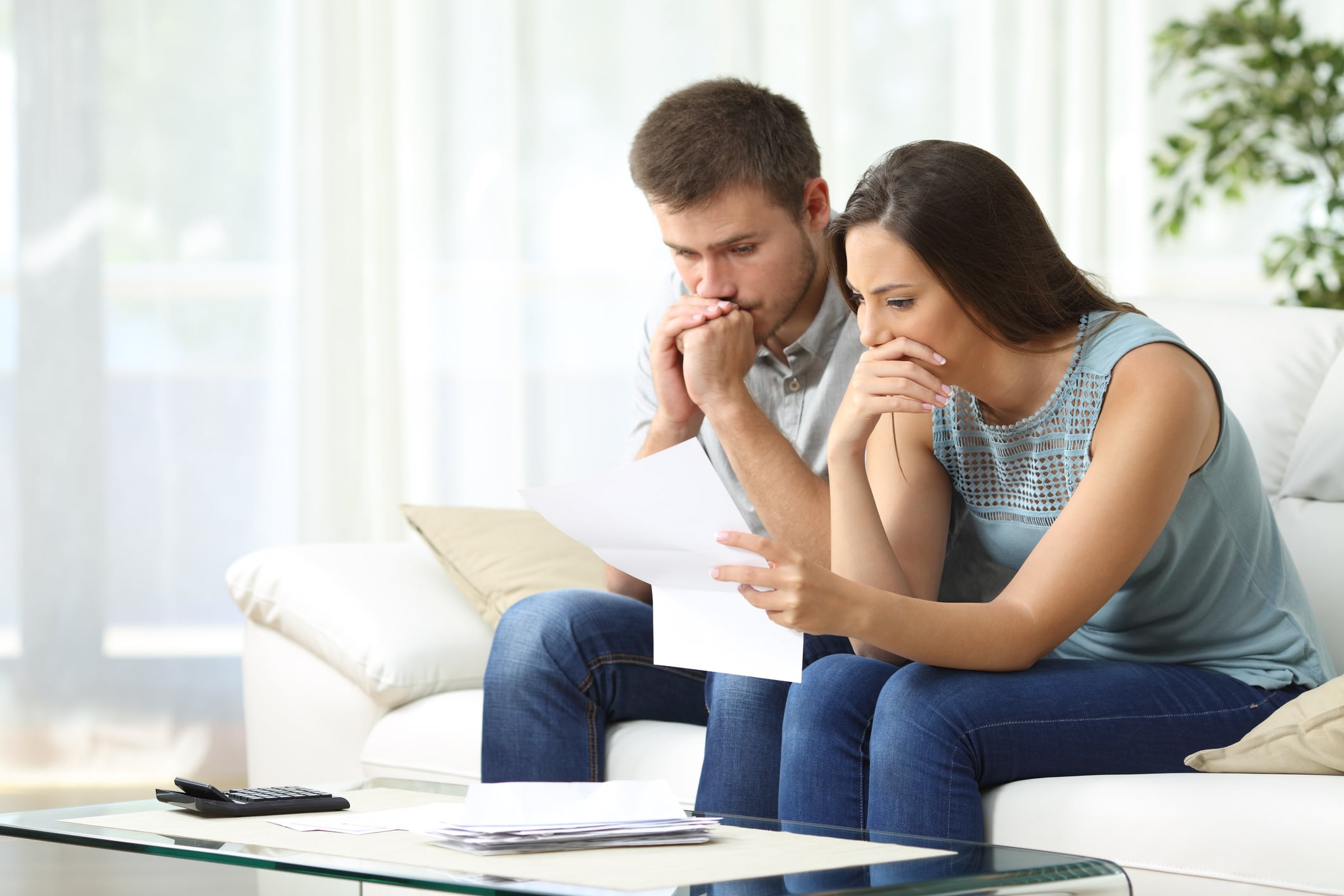 average household credit card debt. Worried couple reading an important notification in a letter sitting on a couch in the living room at home.