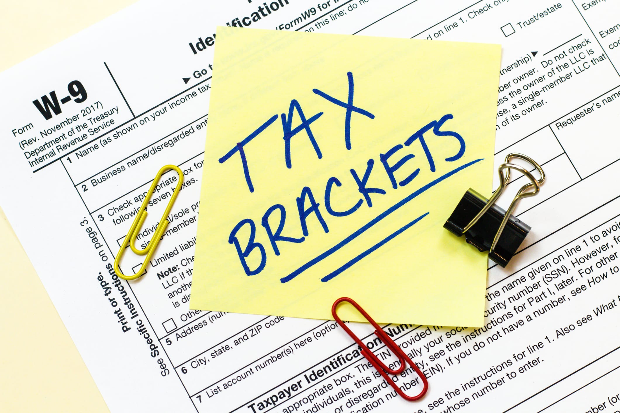 Tax Brackets written on a yellow sticky note on top of tax forms.