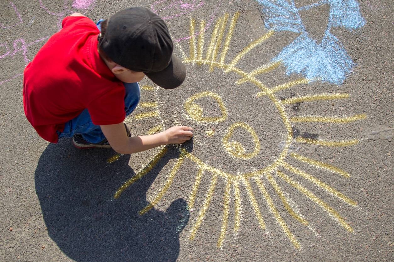 activities for kids - boy draws with chalk on the pavement the sun.