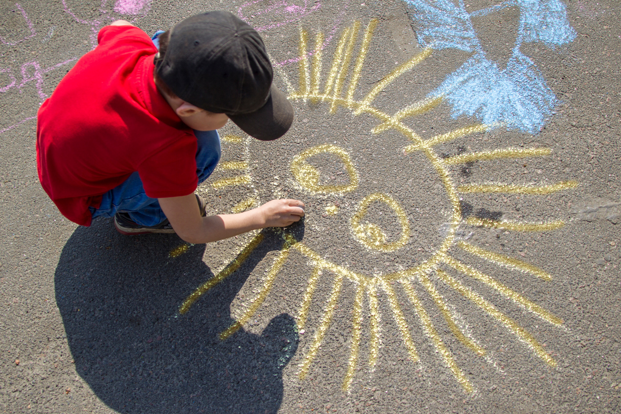 activities for kids - boy draws with chalk on the pavement the sun.