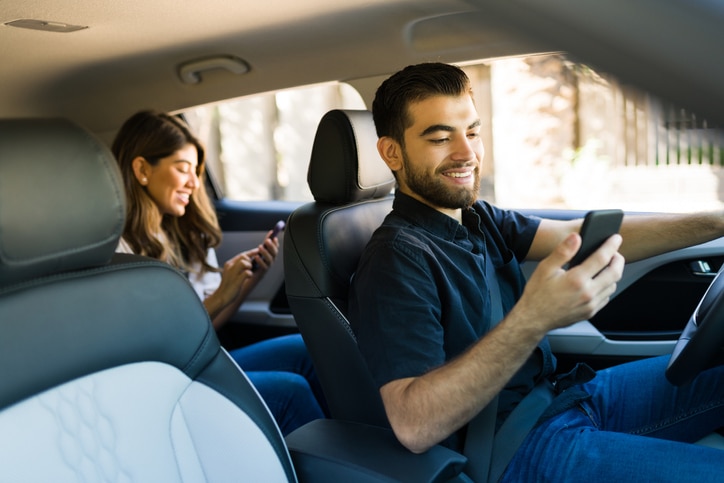 Cheerful side hustles driver looking at the GPS map on the smartphone while taking a woman to a destination using a rideshare app
