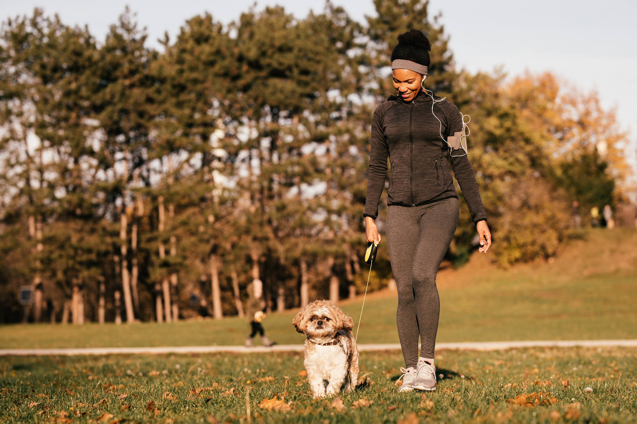 black woman with dog walking and listening to music outdoors, caring for her mental health.